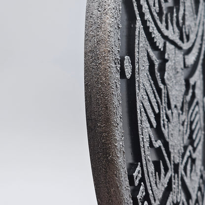 Detail einer runden, schwarz gravierten Wanddeko aus Holz mit rauer Struktur.