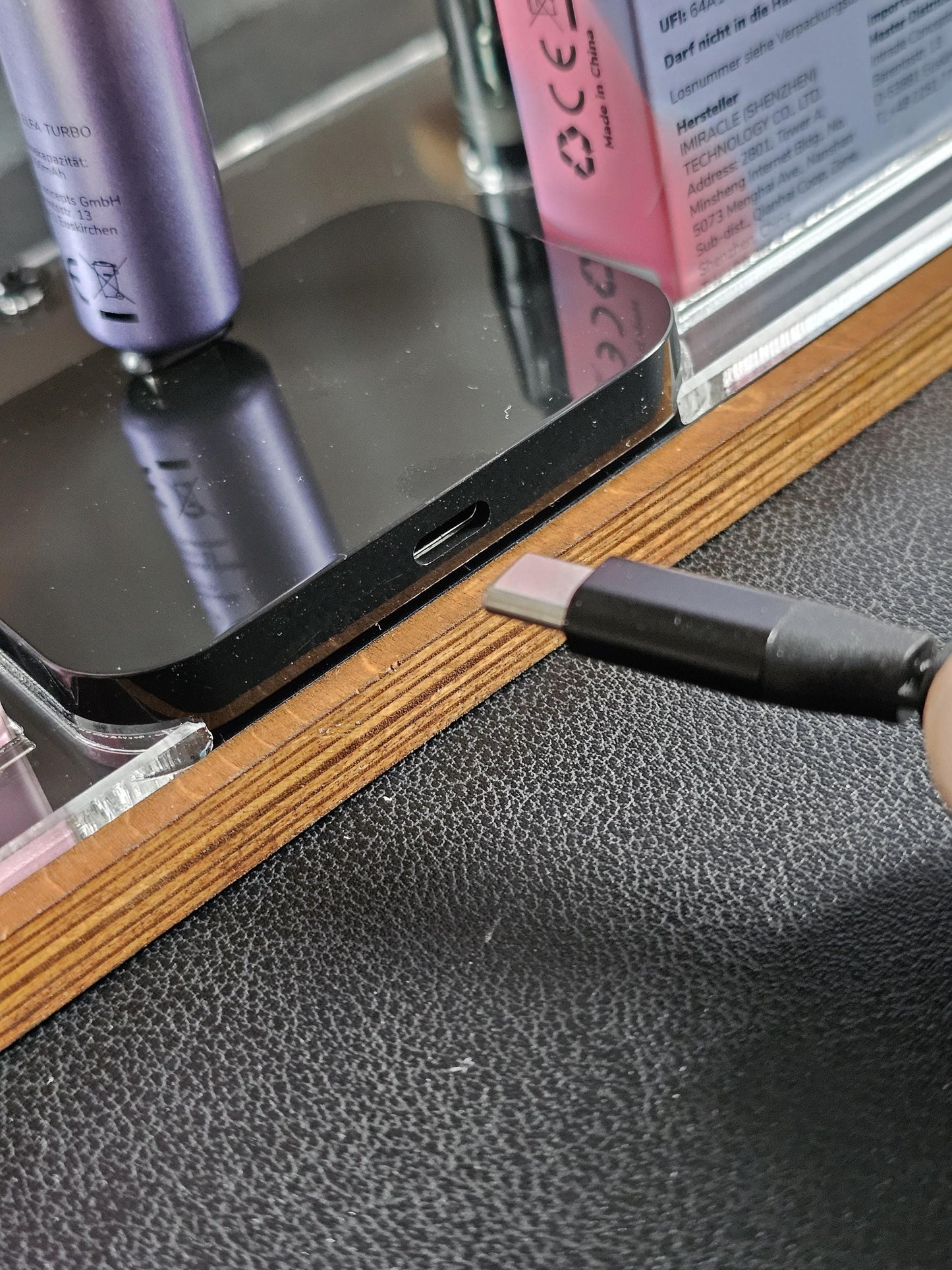 USB-C Kabel wird vor ein schwarzes elektronisches Gerät auf einem Holzständer gehalten