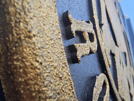 Nahaufnahme einer rauen, schwarzen, lasergravierten Oberfläche mit erhabenen Buchstaben
