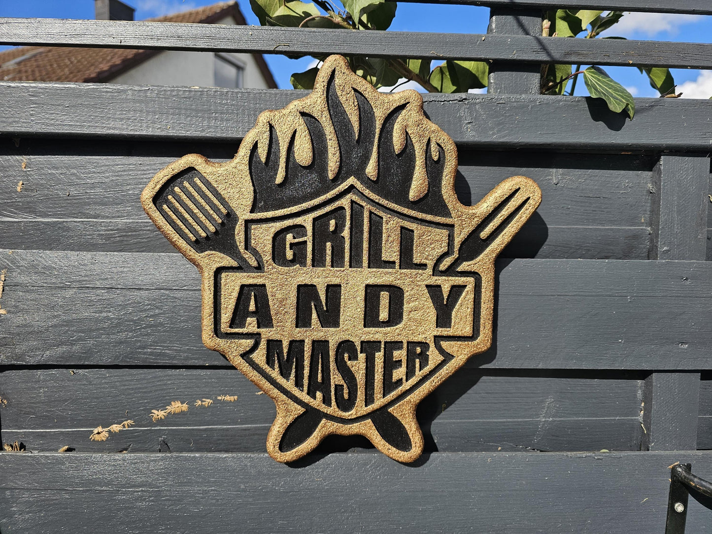 Personalisierte Grillmeister-Holzschild mit Flammenmotiv, Spatel und Gabel an einem Zaun