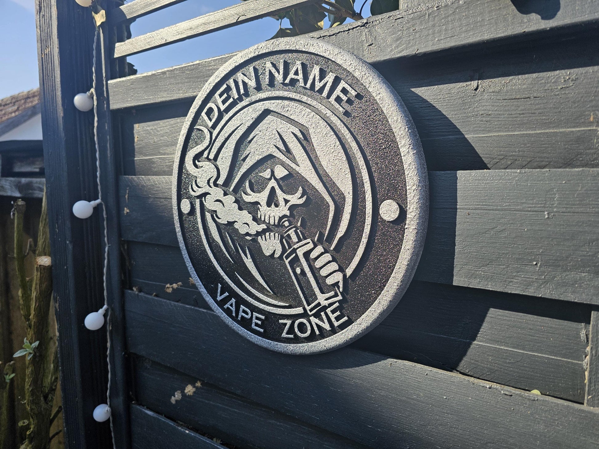 Metallschild mit Sensenmann, der dampft, Gravur 'Dein Name Vape Zone', an Holzzaun