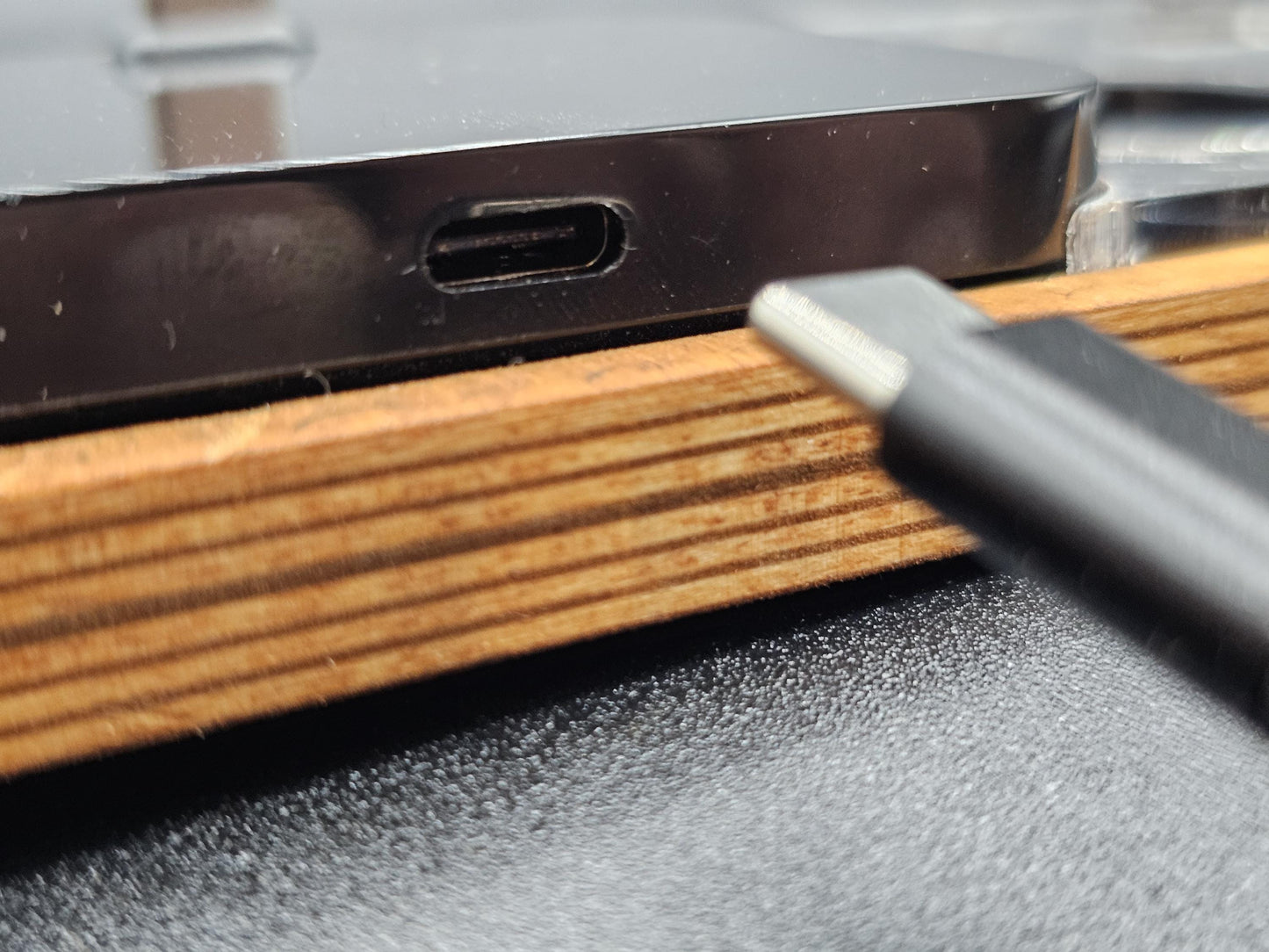 Nahaufnahme eines USB-C-Anschlusses an einem schwarzen Gerät und USB-C-Kabel auf Holzunterlage