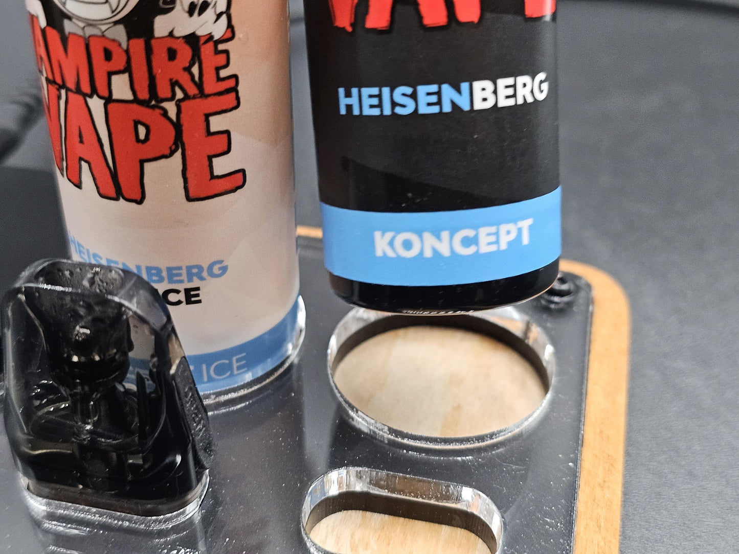 Nahaufnahme von zwei E-Liquid-Flaschen und einem Vaping-Pod in einem Halter aus Holz und Acryl.
